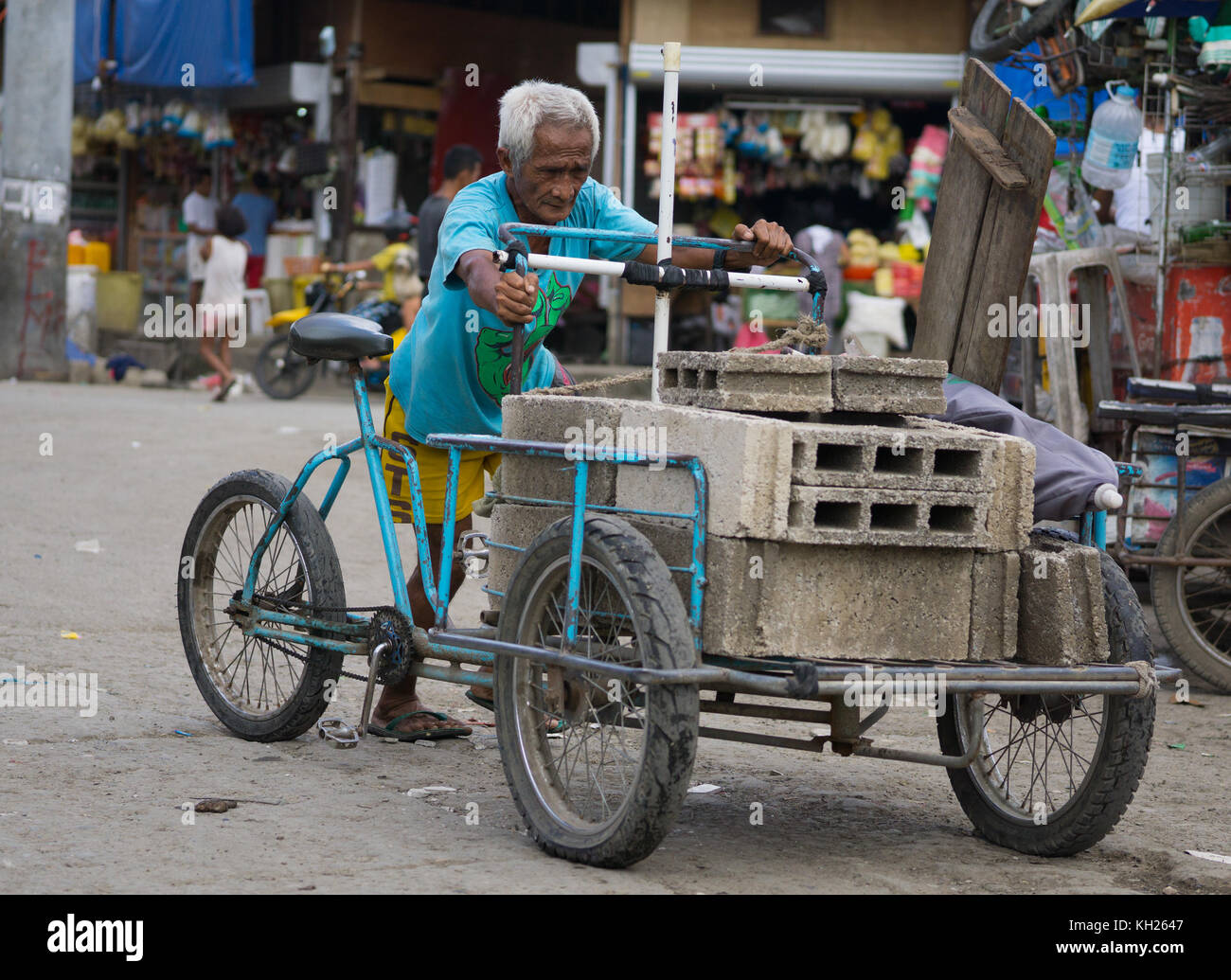 A Filipino man pushing a three wheeled tricycle laden with bricks,Carbon market,Cebu City,Philippines. Stock Photo