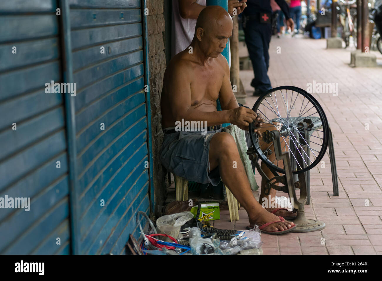 A Filipino man working on the side of a street fixing a bicycle wheel,Cebu City,Philippines Stock Photo