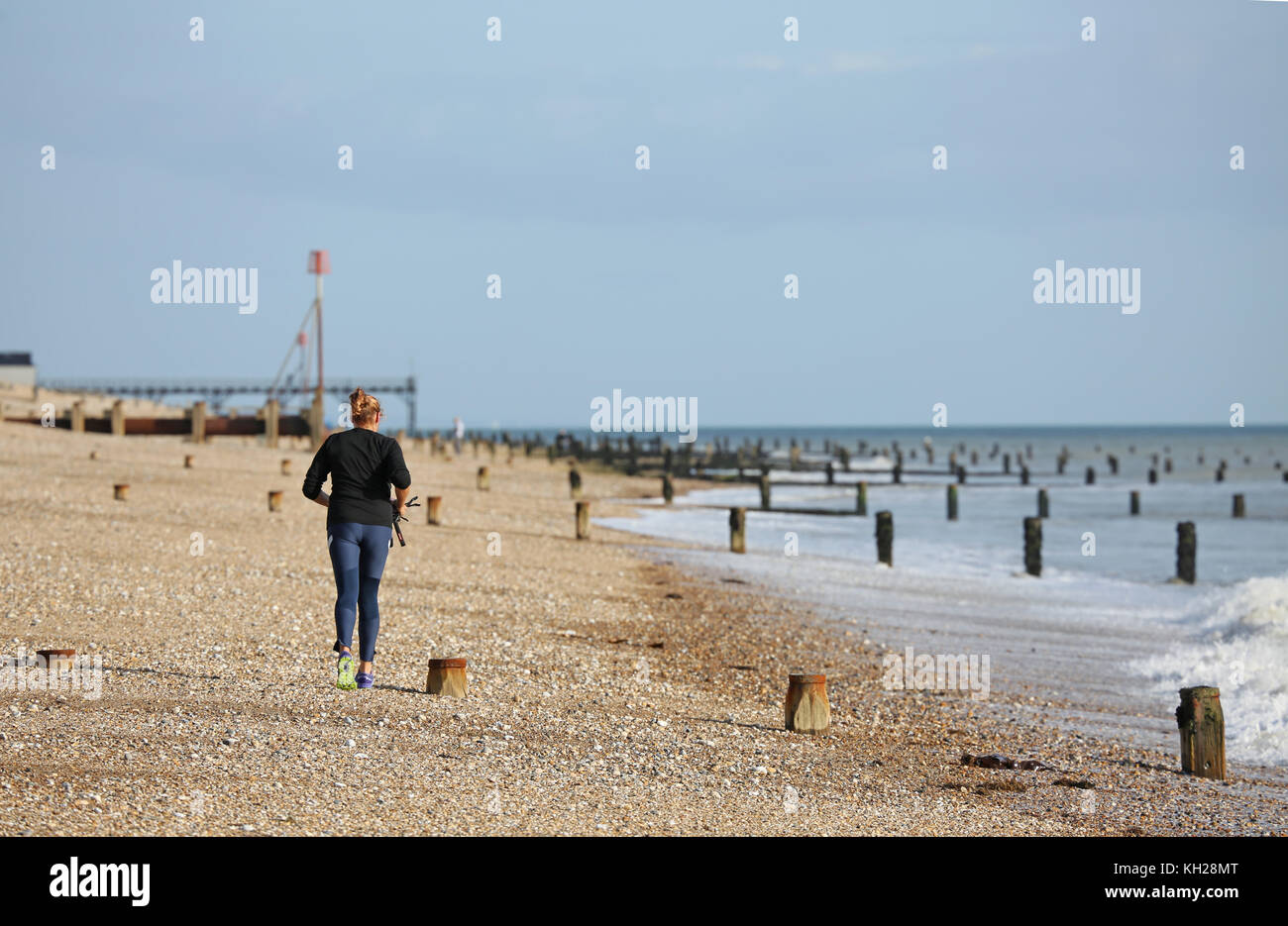 A woman jogs along the shoreline on the beach at Bognor Regis, West Sussex, on a sunny, winter day. Stock Photo