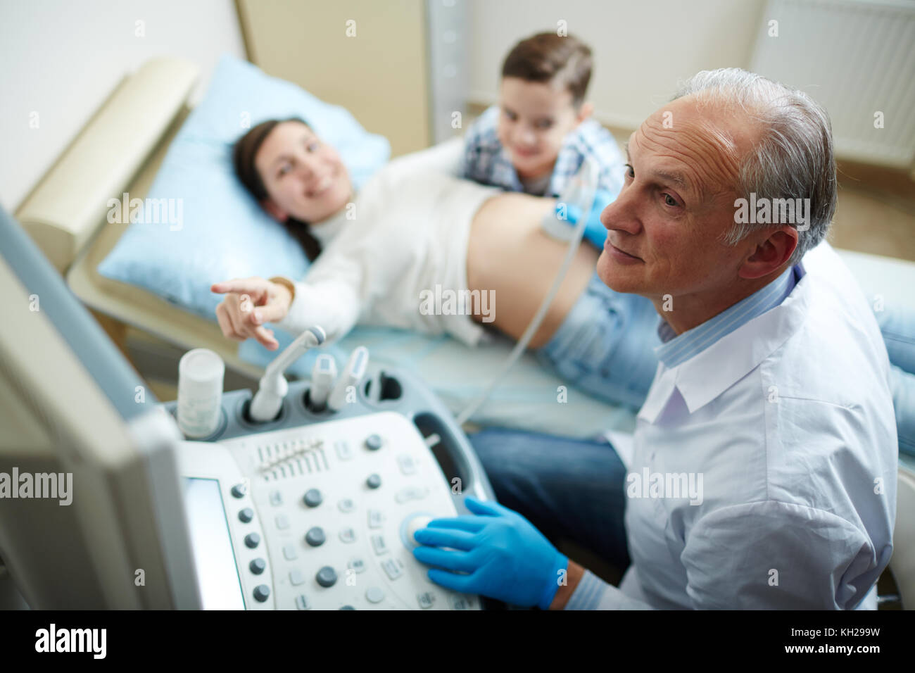 Aged doctor looking at monitor of ultrasound machine during check-up of pregnant woman Stock Photo