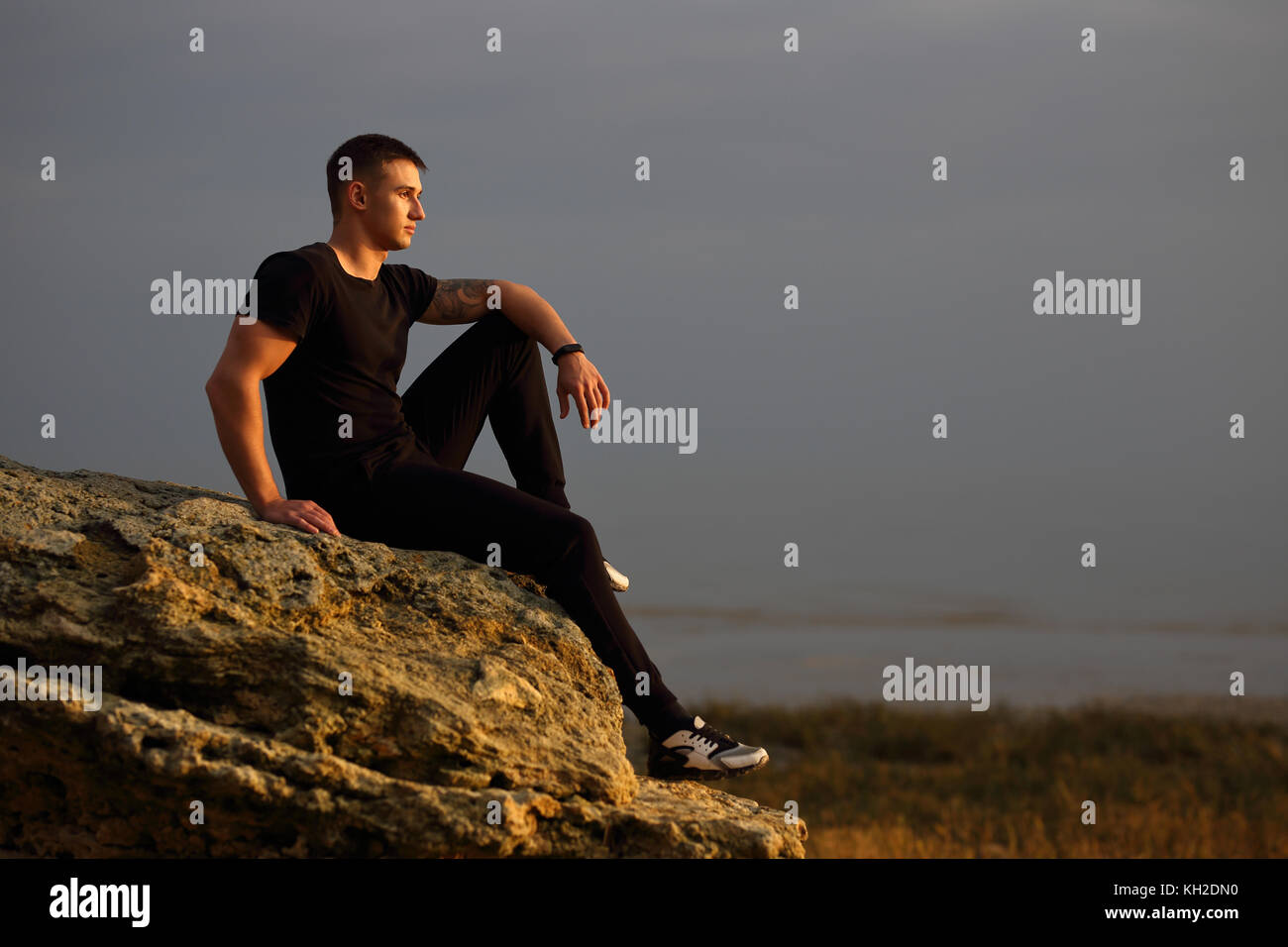 Man sitting on rocky beach in the sunset at the sea Stock Photo Alamy