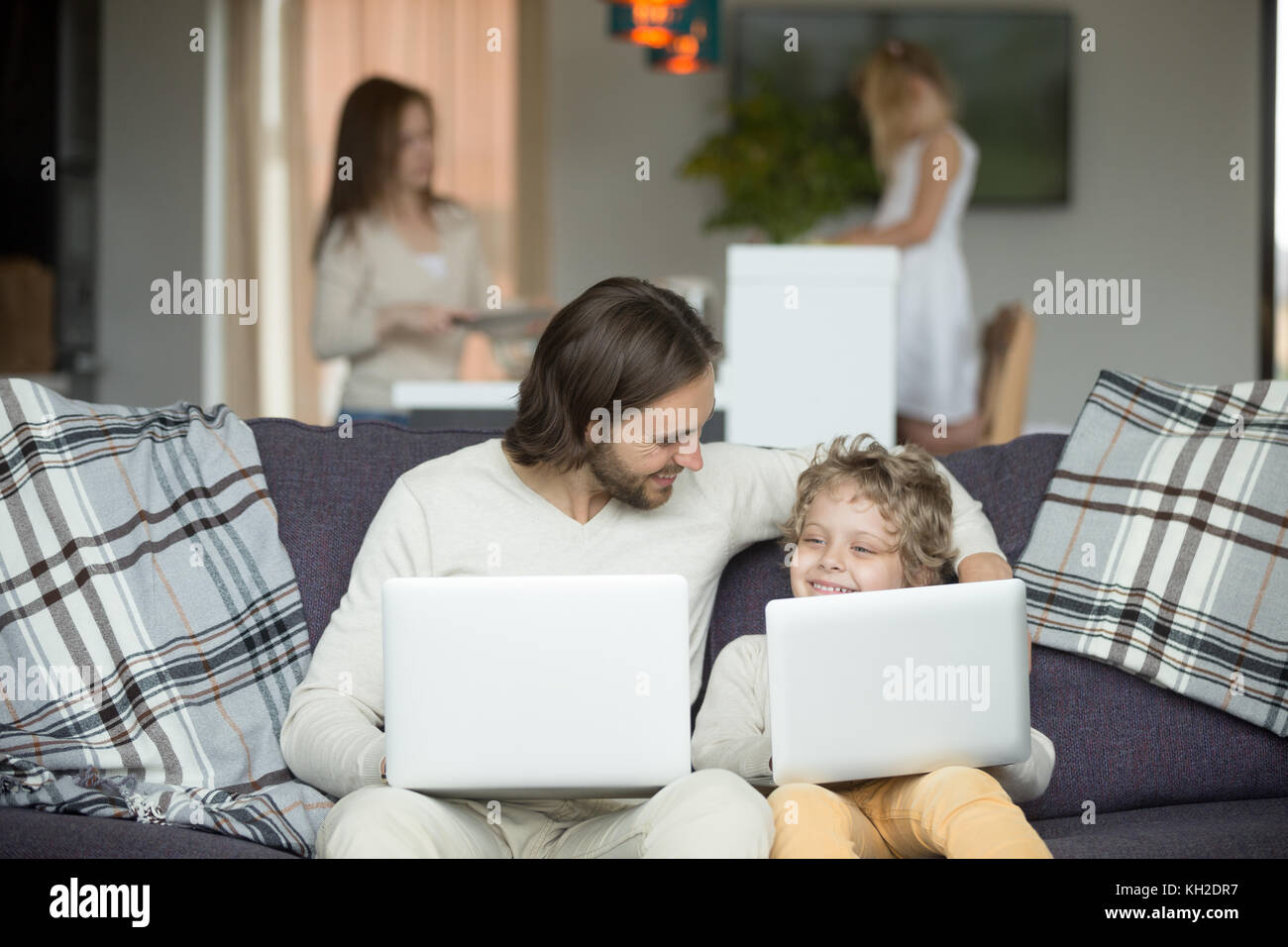 Happy father and son embracing using laptops together at home, smiling dad and boy bonding holding computers sitting on sofa, kid imitating copying da Stock Photo