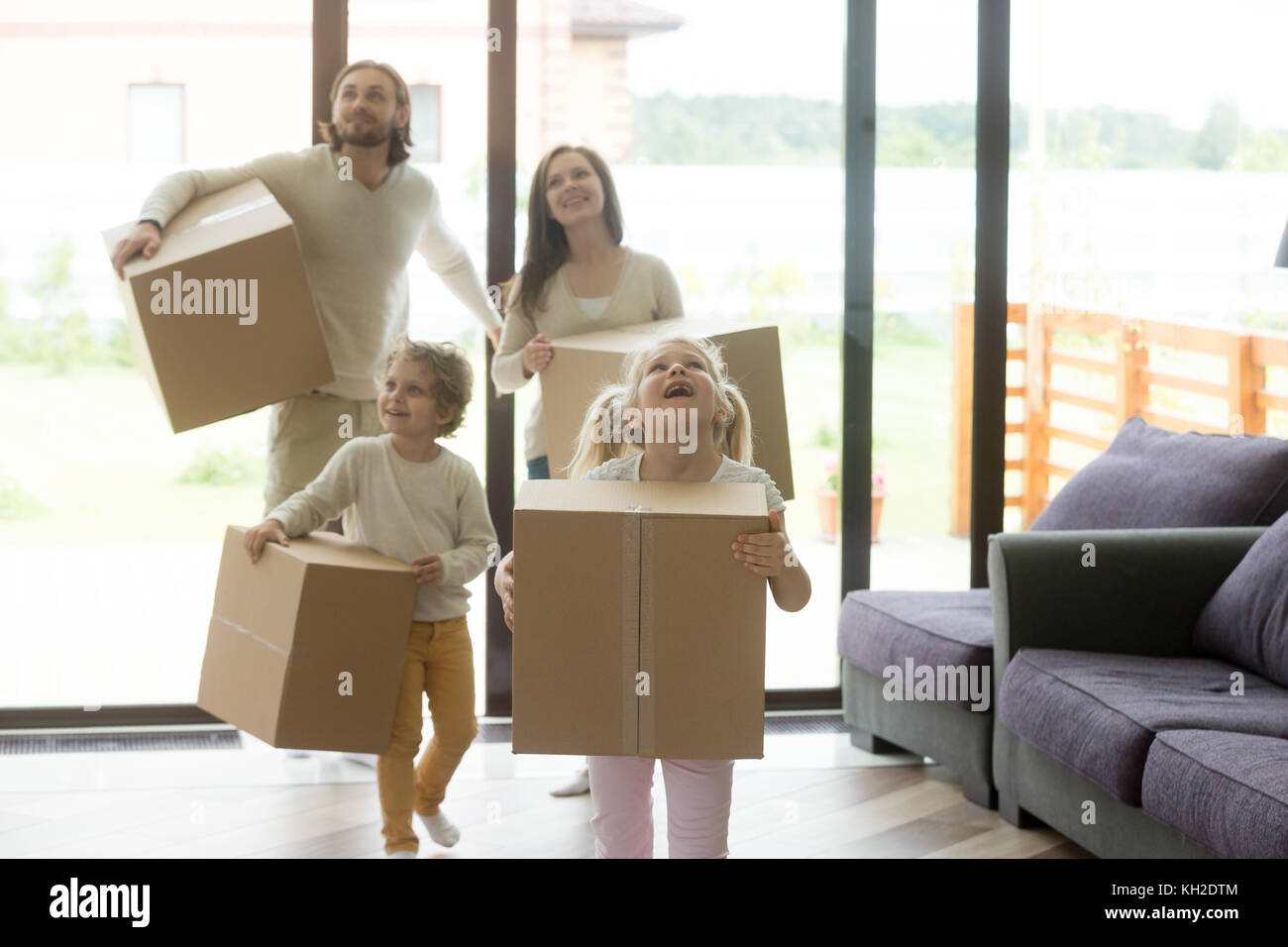 Excited family with children coming into new home on moving day, happy kids and parents looking around holding cardboard boxes entering in big house,  Stock Photo