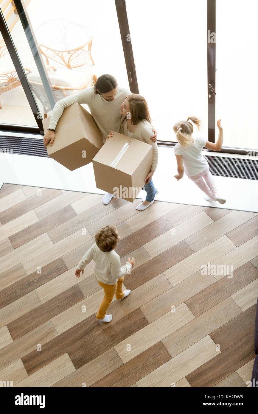 Family and children moving into new home, kids playing running around parents holding boxes standing in house hall together, happy couple with two chi Stock Photo