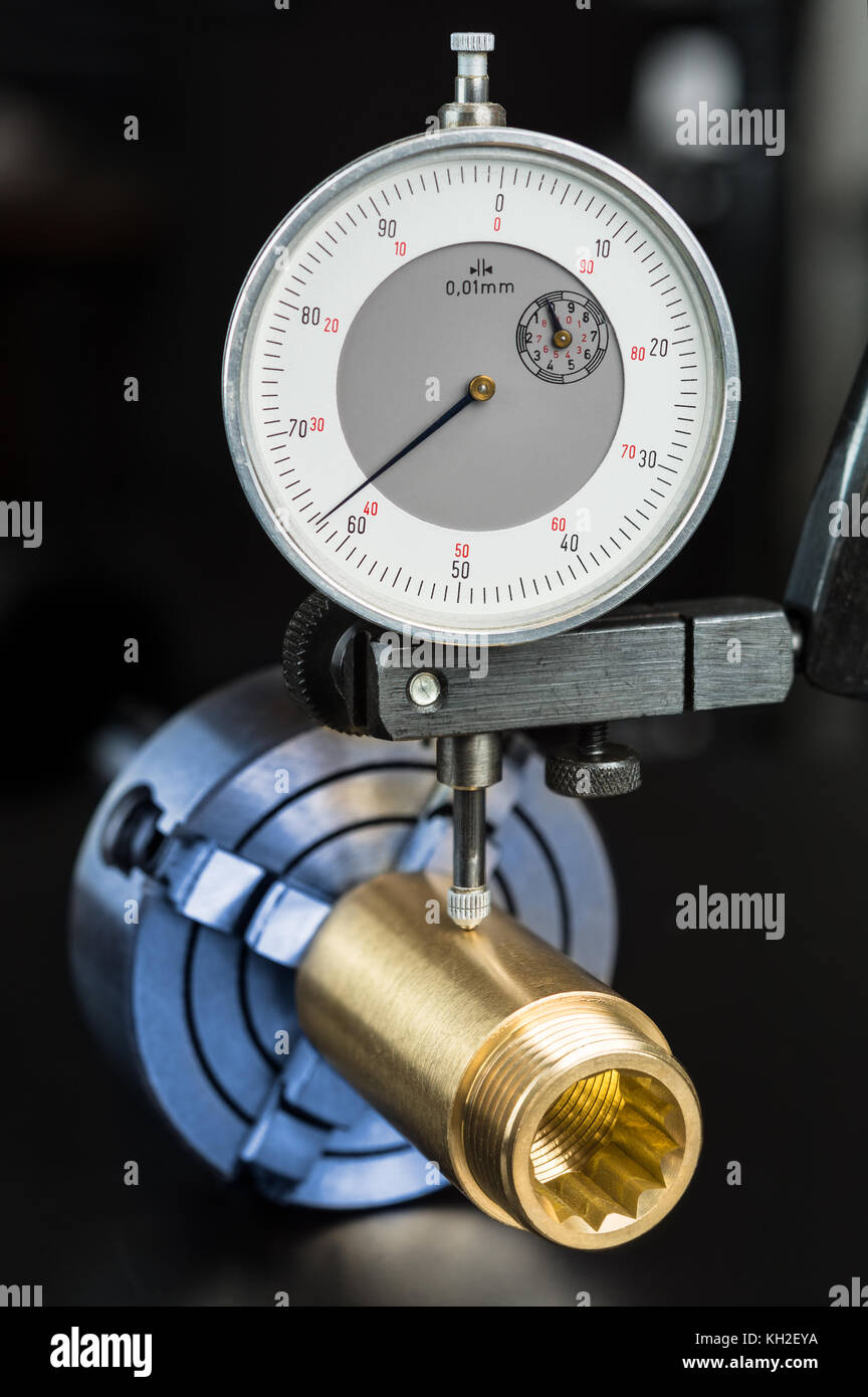 Tolerance measurement of brass workpiece in chuck. Fitting and dial indicator in holder on black background. Engineering, education, industry concept. Stock Photo