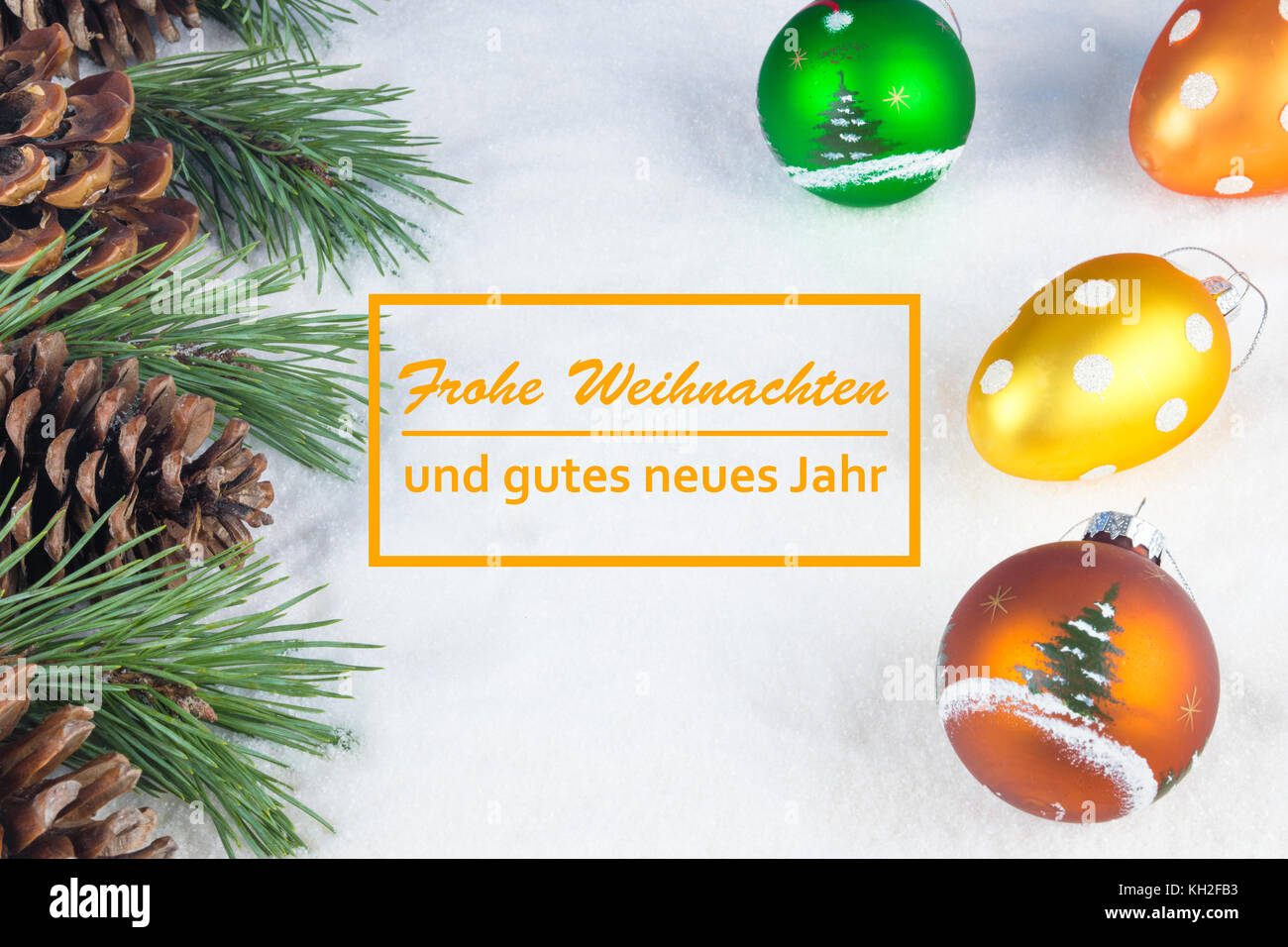 Group of pine trees, some branches and colorful baubles and Christmas balls with text in German "Frohe Weihnachten und gutes neues Jahr" in white snow Stock Photo