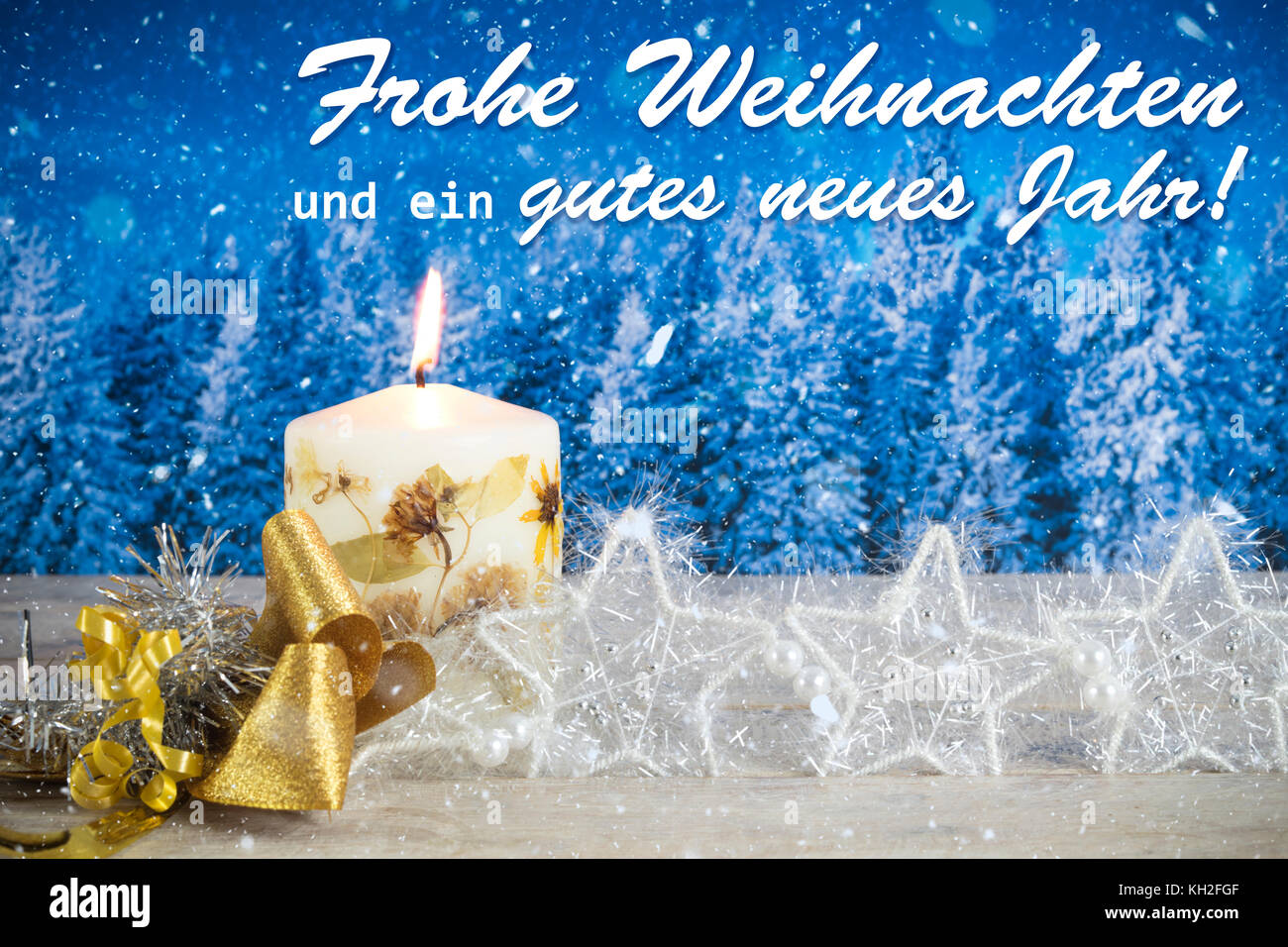 Christmas decoration with candle, golden bow, silver stars, with text in German 'Frohe Weihnachten und ein gutes neues Jahr' in a blue forest backgrou Stock Photo