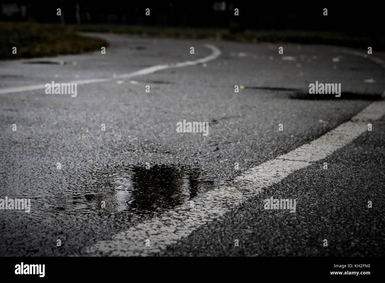 Asphalt track at an old school stadium during a rain with a puddle in the foreground. Dark autumn day Stock Photo