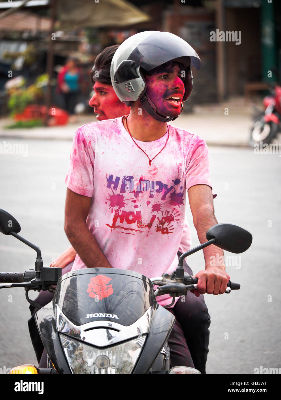Young Nepali men covered with coloured powder return home on a scooter after celebrating the Hindu festival Holi in Pokhara, Nepal Stock Photo