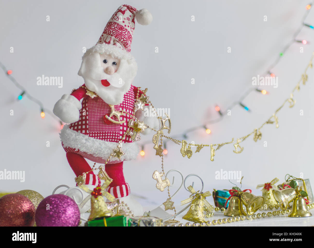 Santa Claus decoration stuffed toy, on a white background and surface, with colorful bokeh lights and christmas decoration in the background Stock Photo