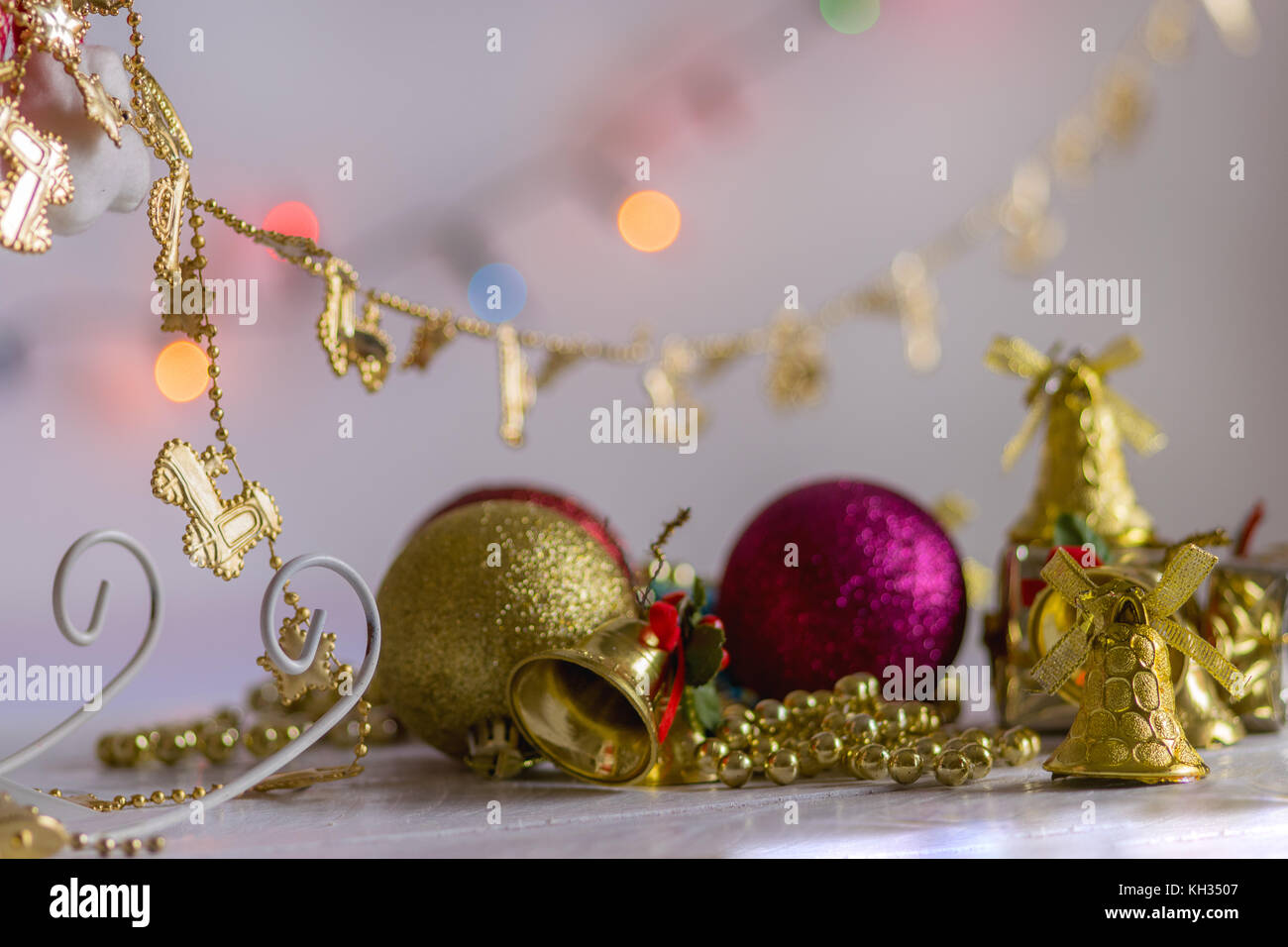Christmas Decoration, gifts, chains, bells and colorful reflective balls, on top of a white wood surface and white background, with bokeh background Stock Photo