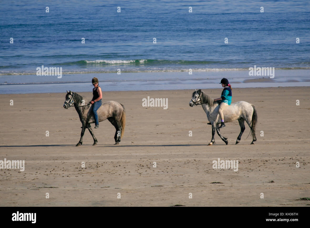 Two girls riding horses on a sunny summer day on a sandy Keel Beach in Achill Island, County Mayo, Ireland Stock Photo
