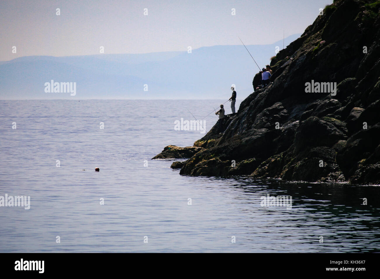 Men angling from the rocks at the feet of Moyteoge Head sea cliff at Keem Bay, Achill Island, County Mayo, Ireland Stock Photo
