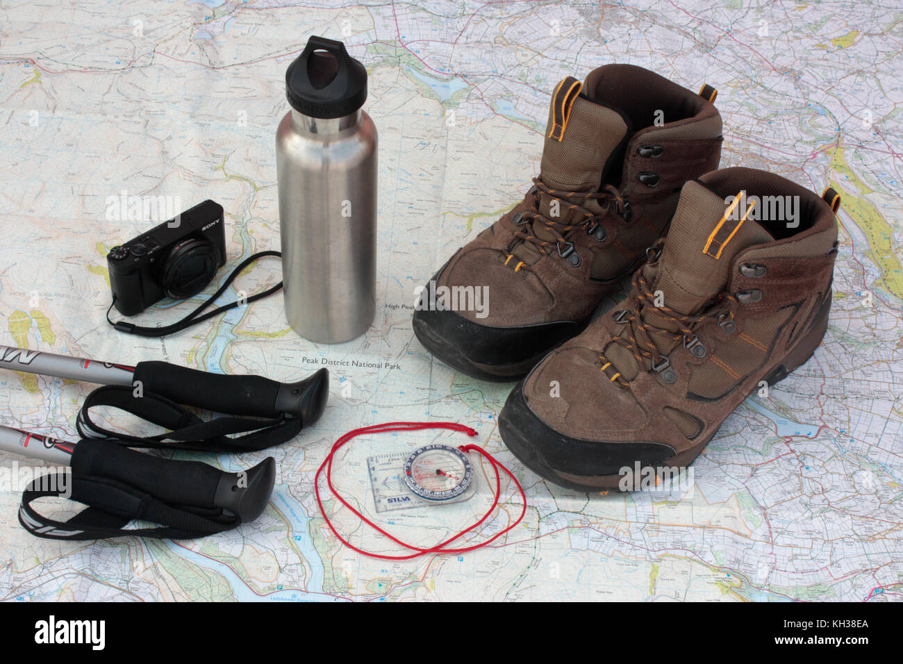 Trekking in the UK. Walking poles, digital camera, water flask, compass and hiking boots set out on a map of Peak District National Park Stock Photo
