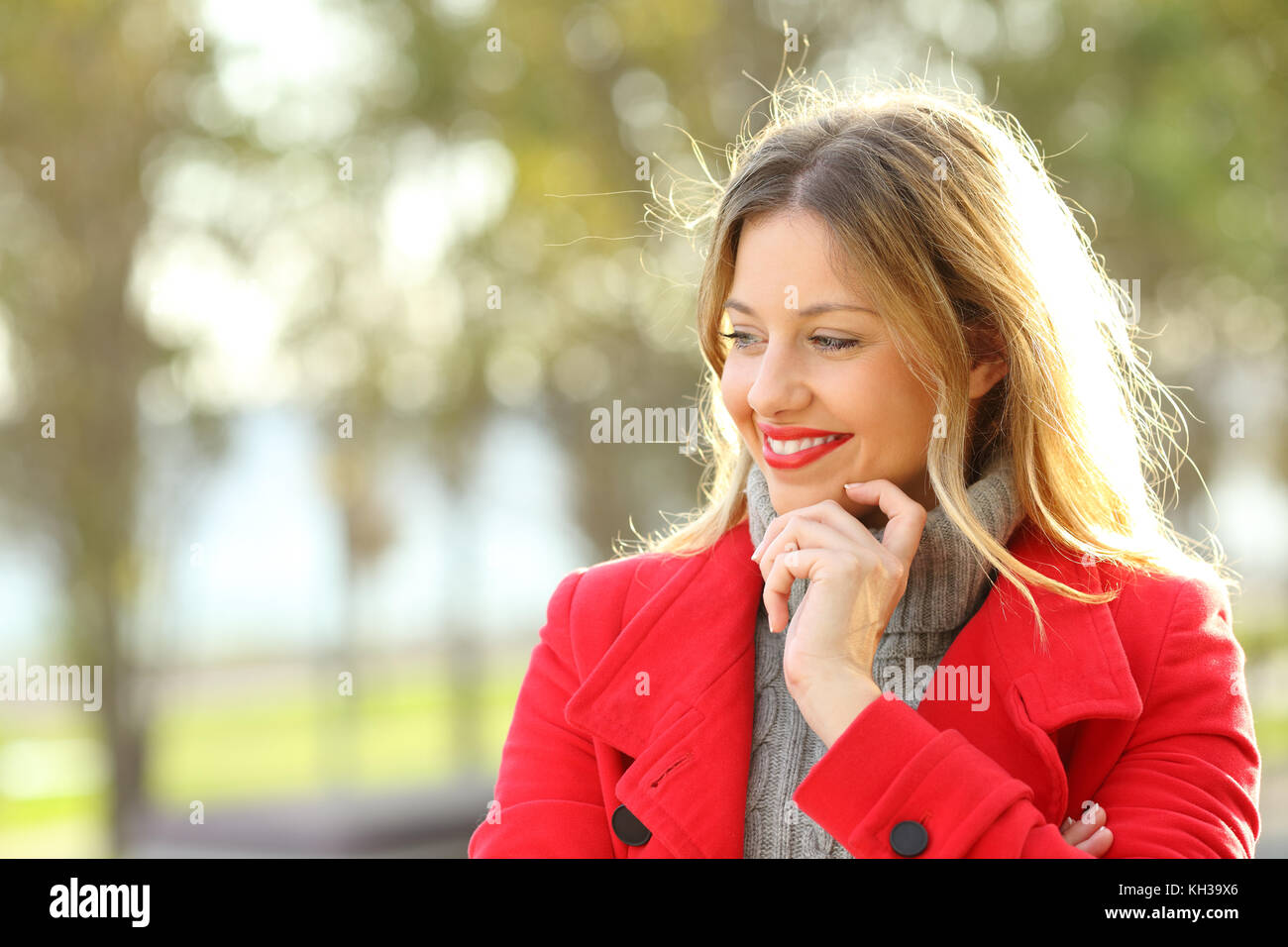 Happy pensive lady wearing a red jacket looking at side in a park in winter Stock Photo
