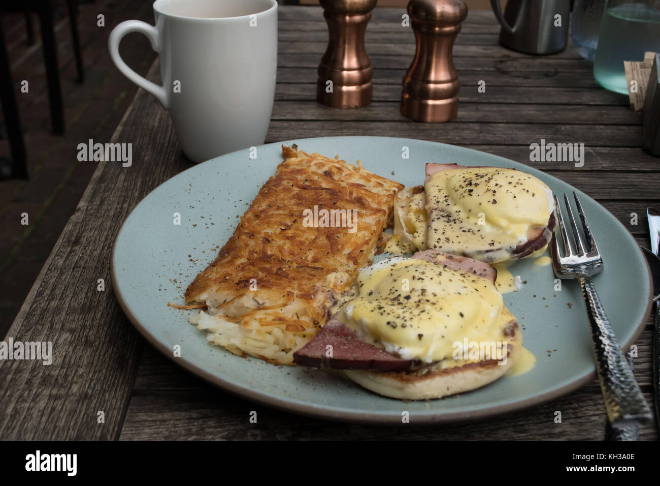 Casual breakfast of Eggs Benedict an outdoor cafe. Traditional place setting with cloth napkin, copper fixtures and a hot cup of coffee- delicious Stock Photo