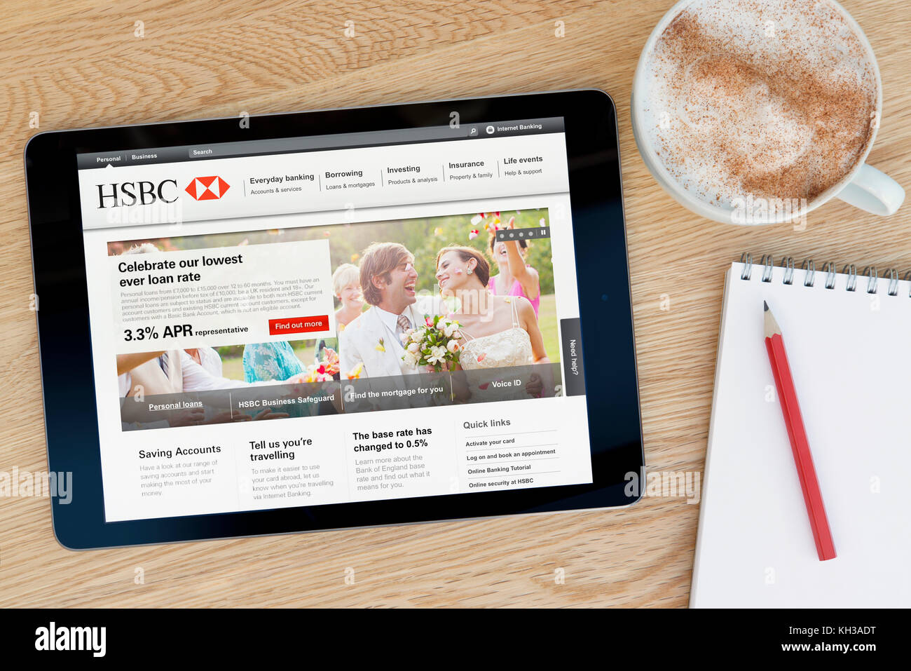 The HSBC bank website features on an iPad tablet device which rests on a wooden table beside a notepad and pencil and a cup of coffee (Editorial only) Stock Photo