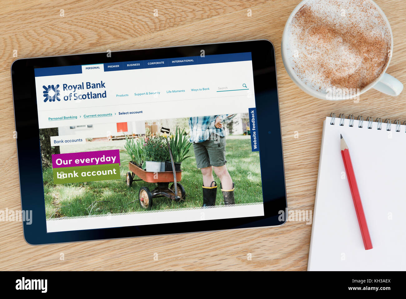 The RBS bank website features on an iPad tablet device which rests on a wooden table beside a notepad and pencil and a cup of coffee (Editorial  only) Stock Photo