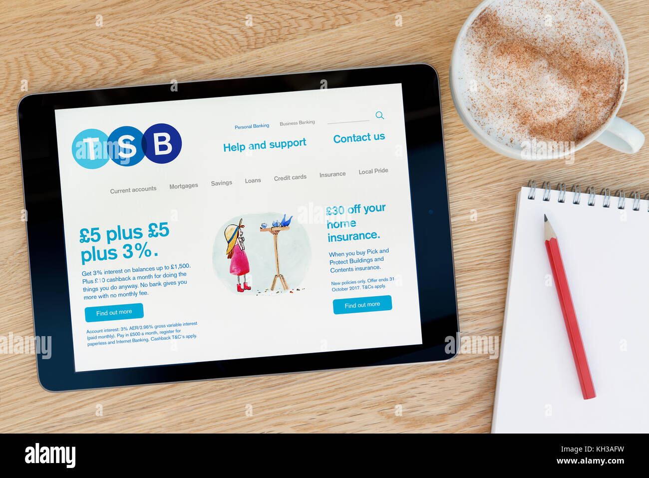 The TSB bank website features on an iPad tablet device which rests on a wooden table beside a notepad and pencil and a cup of coffee (Editorial only) Stock Photo