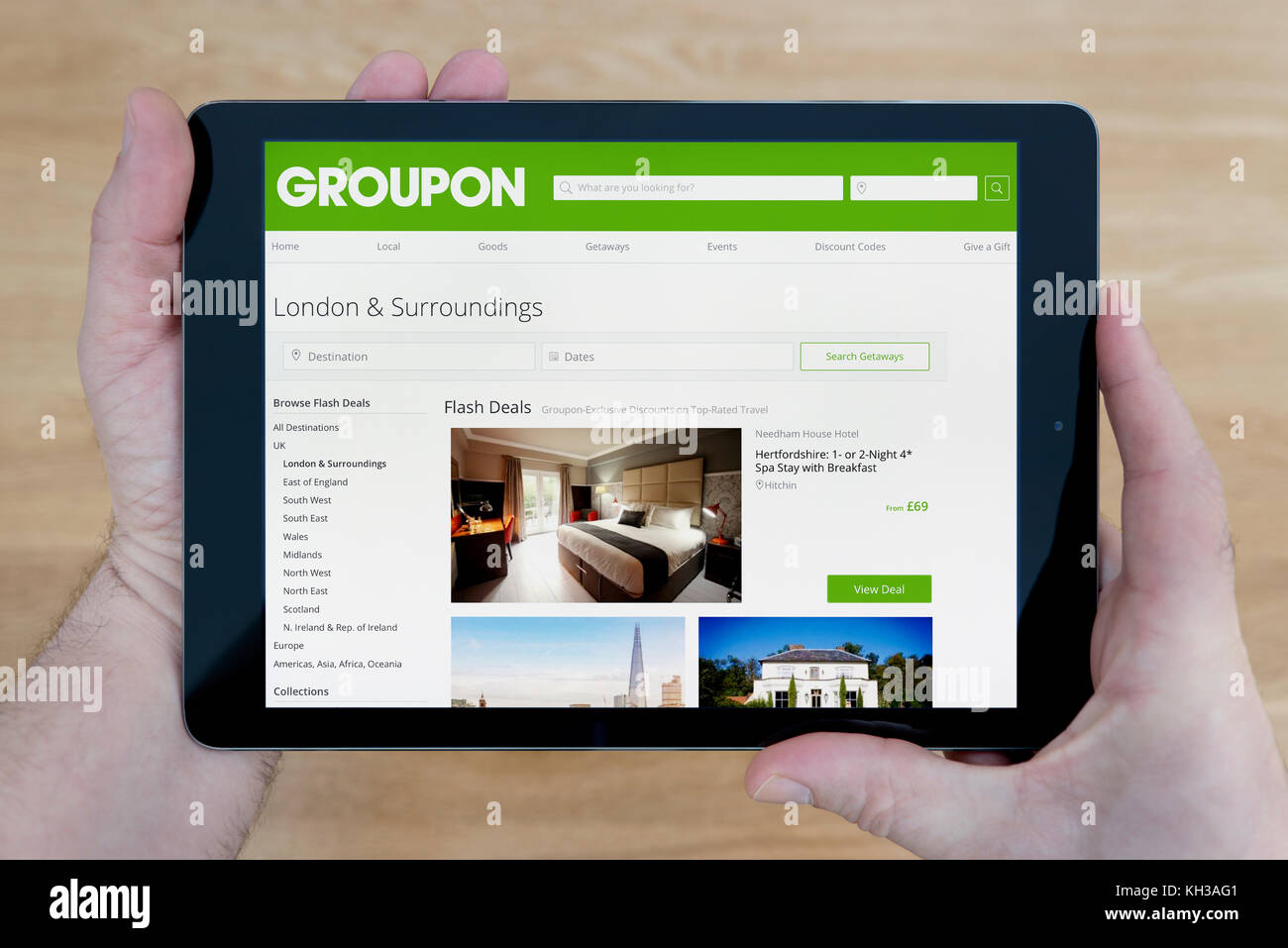 A man looks at the Groupon website on his iPad tablet device, shot against a wooden table top background (Editorial use only) Stock Photo