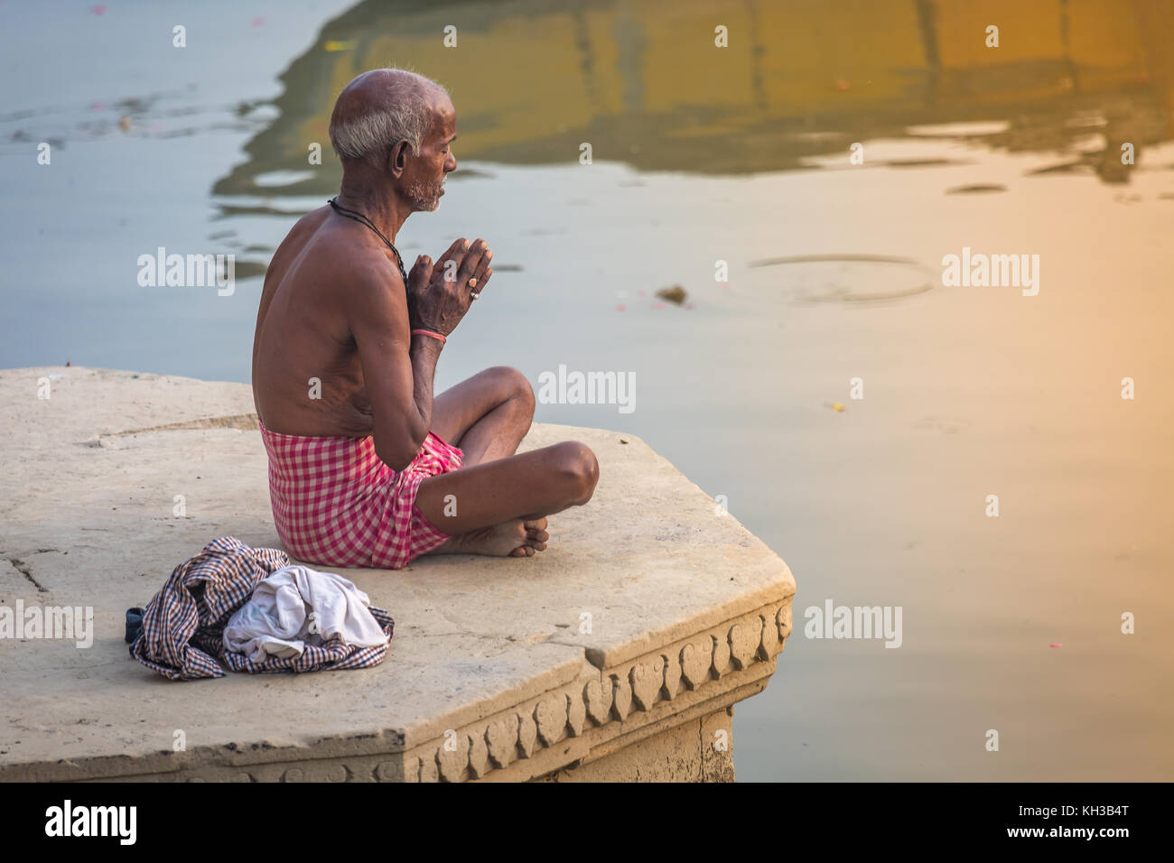 Old man performs early morning meditation yoga at sunrise at the Ganges river ghat at Varanasi India. Stock Photo