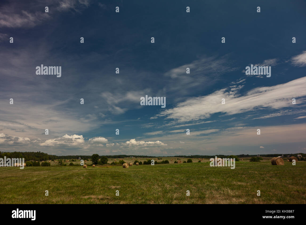 Blue skies over a large field of green with hay bales Stock Photo - Alamy
