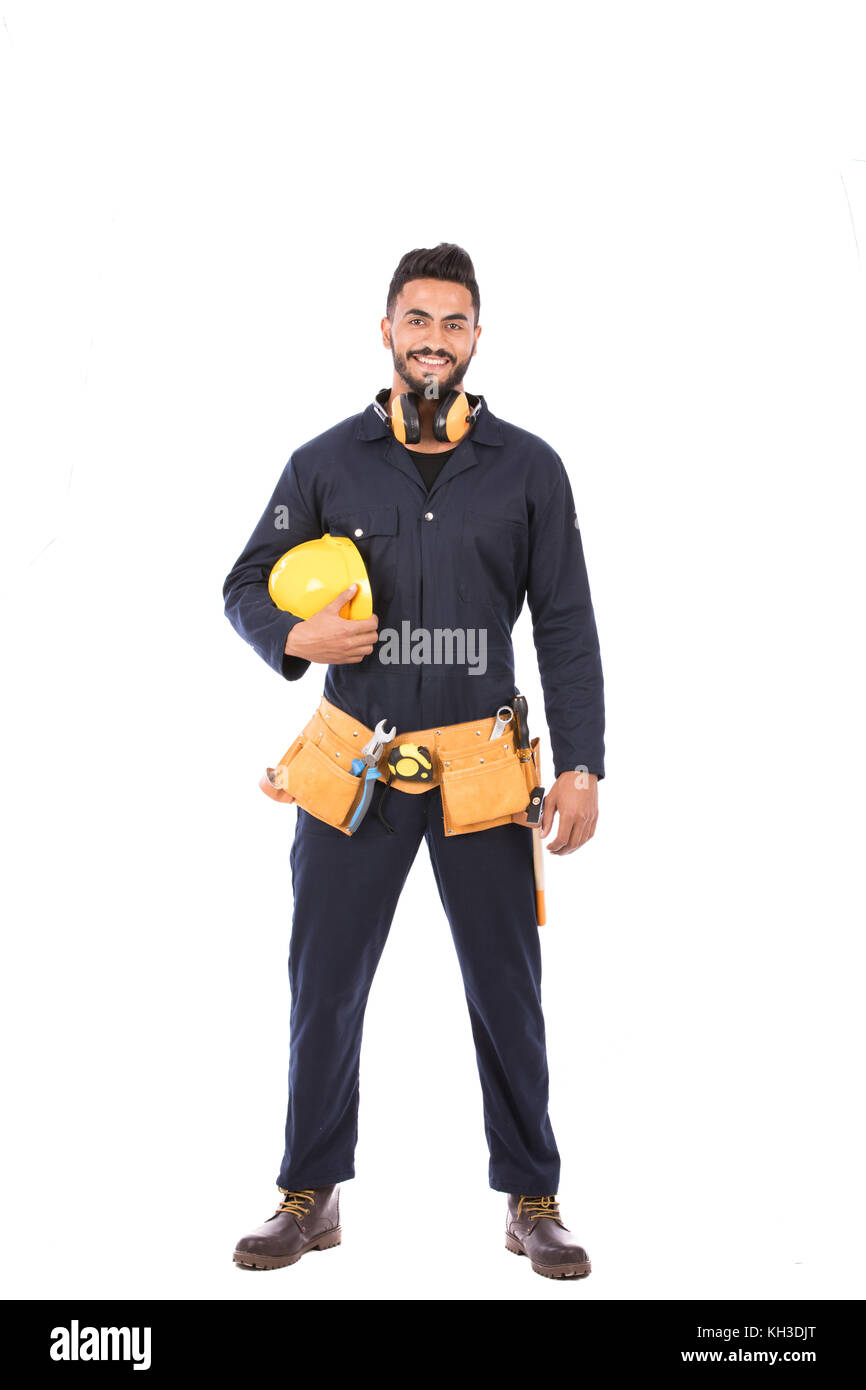Full length shot of happy beard worker smiling and holding a yellow helmet, guy wearing dark blue workwear and belt equipment, isolated on white backg Stock Photo