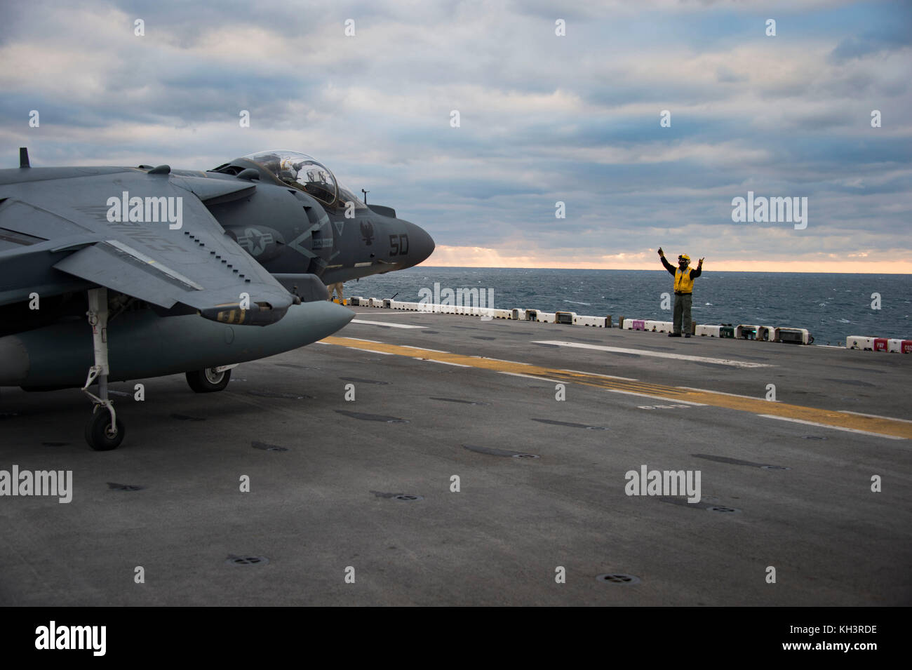 A Sailor directs an AV-8B Harrier II jet, attached to Marine Medium Tiltrotor Squadron 162, on the flight deck of the a Stock Photo