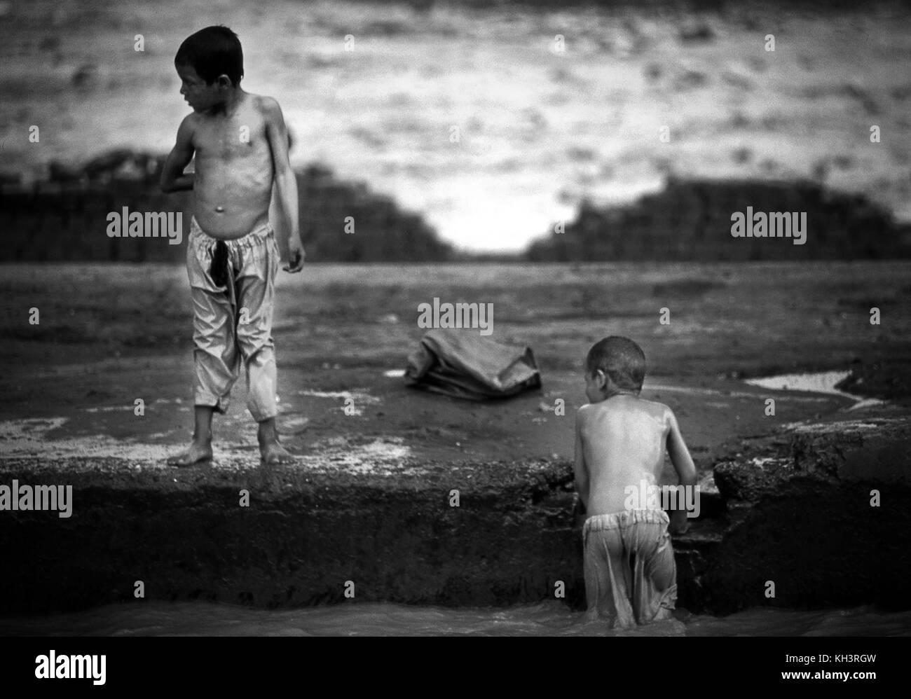 Two afghan refugee boys play and bathe in a water channel at the city of Peshawar, Pakistan. Image of a brick factory where the workers are mainly afghan refugees near Peshawar, Pakistan. Date: 8/2000. Photographer: Xabier Mikel Laburu Stock Photo