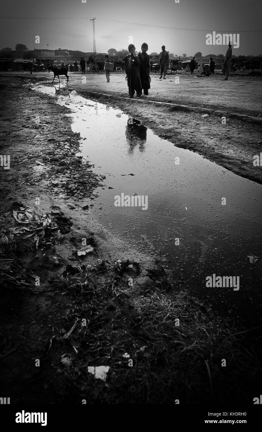 Two kids stand by a dirty water puddle in the fruit market refugee camp in Rawalpindi, Pakistan. Image of a brick factory where the workers are mainly afghan refugees near Peshawar, Pakistan. Date: 8/2000. Photographer: Xabier Mikel Laburu Stock Photo