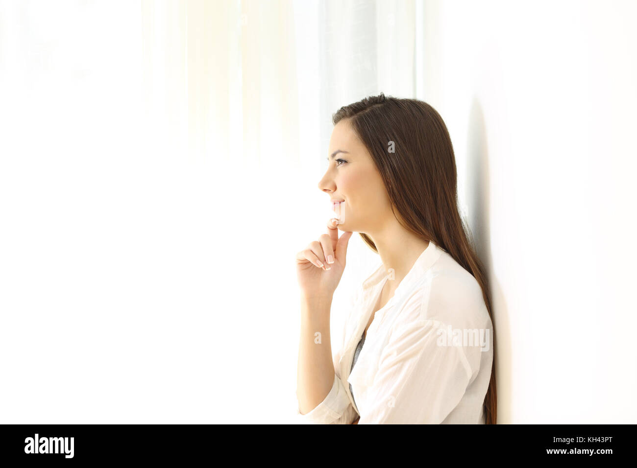 Side view portrait of a woman thinking leaning on a wall at home isolated on white at side Stock Photo