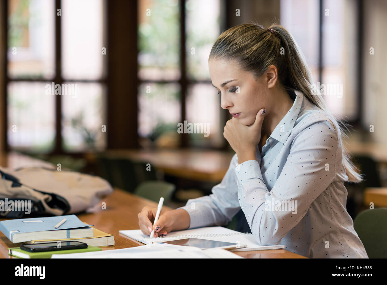 Efficient female student at the library, she is sitting at desk and studying, education and self improvement concept Stock Photo