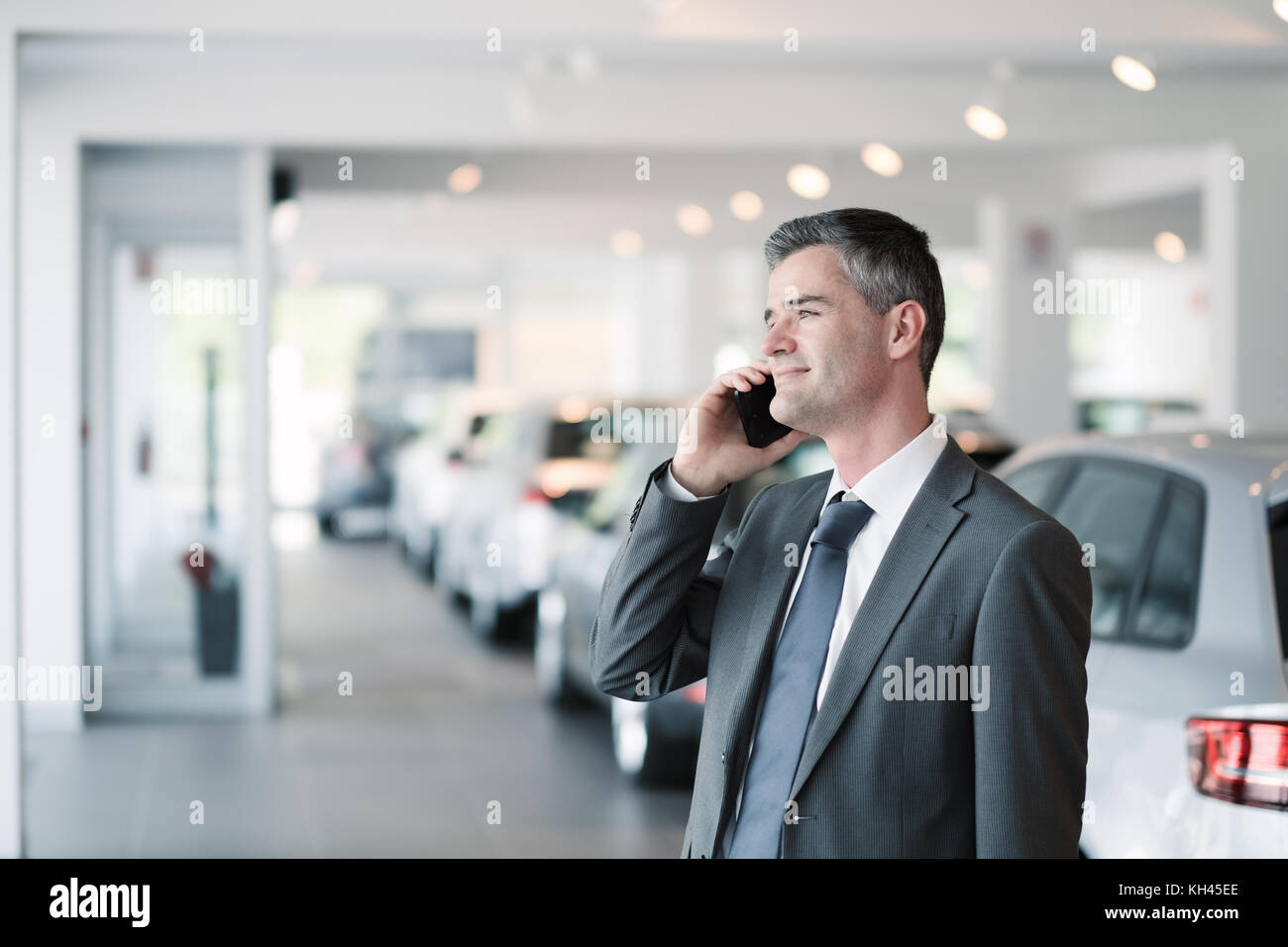 Businessman having a phone call at the car showroom, car dealership