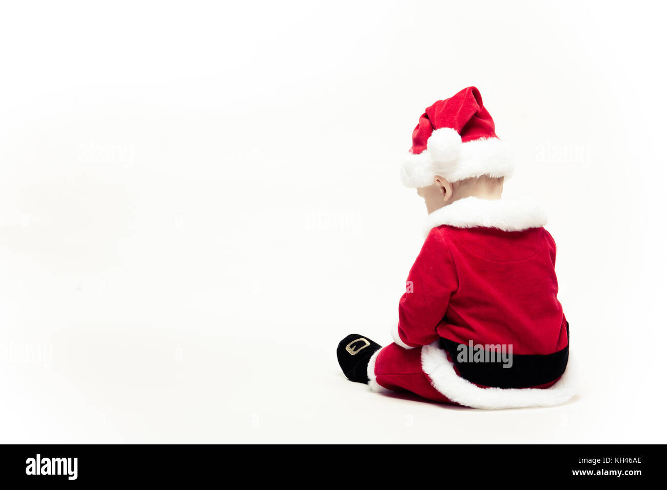 Santa Claus baby in red christmas clothes sits with his back isolated on white Stock Photo