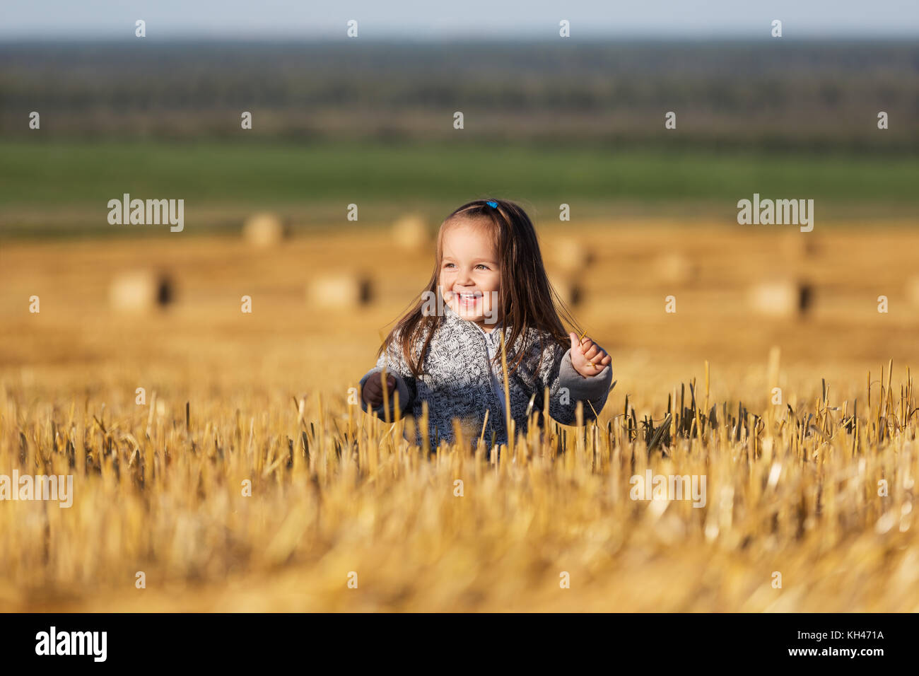 Happy 2 year old girl walking in a summer harvested field Stock Photo