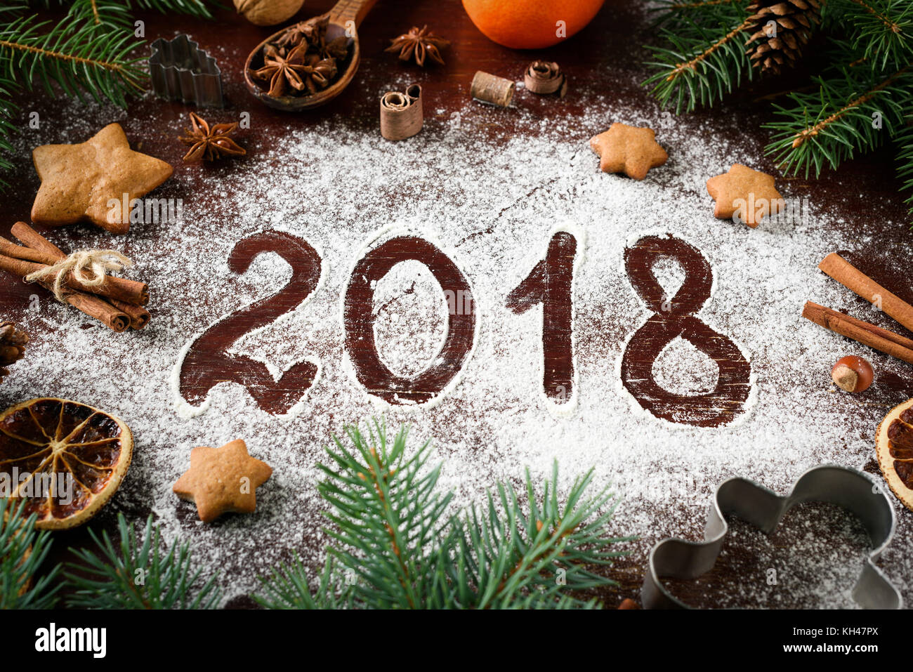 New Year 2018 written on flour and Christmas Decorations Gingerbread cookies, cinnamin, oranges, spices, nuts and cookie cutters on wooden background. Stock Photo