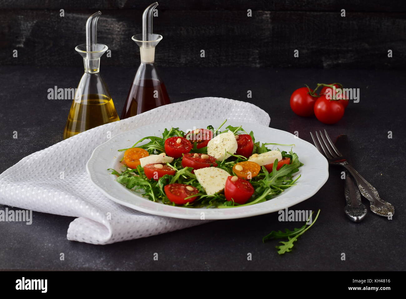 Traditional Italian salad with cherry tomato, rucola, mozzarella, olive oil wine vinegar on a white plate on a grey abstract background. Stock Photo