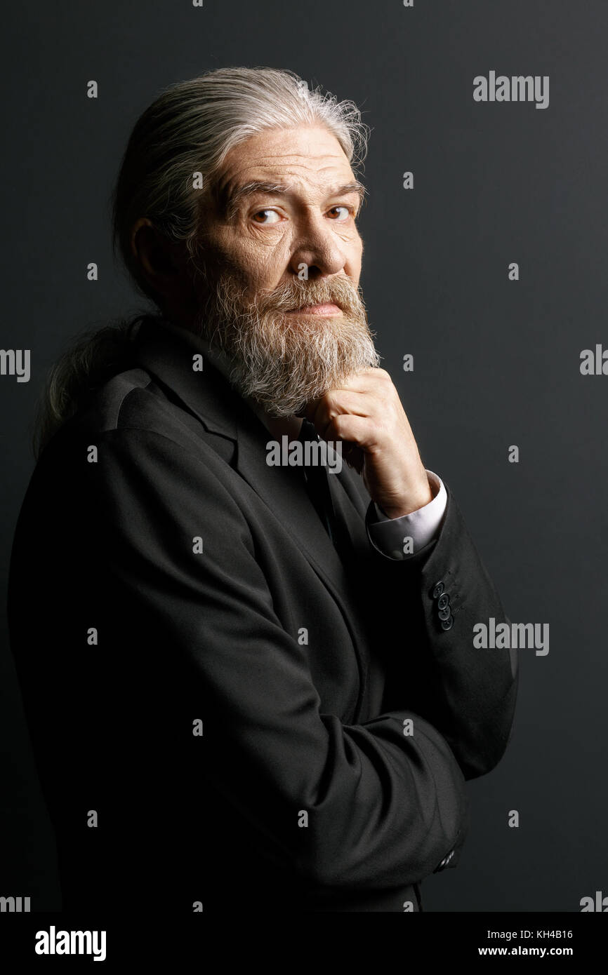 Old man with long grey hair and beard on black background. Stock Photo
