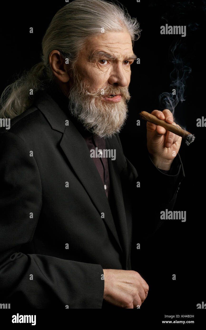 Old man with long grey hair holding cigar. Stock Photo