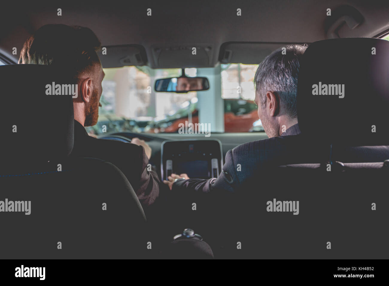 Vehicle dealer and buyer sitting inside a new car in auto showroom. Stock Photo