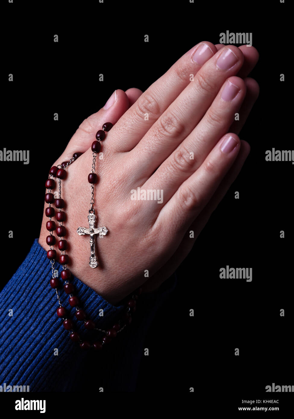 Female hands praying holding a rosary with Jesus Christ in the cross or Crucifix on black background. Woman with Christian Catholic hand faith Stock Photo