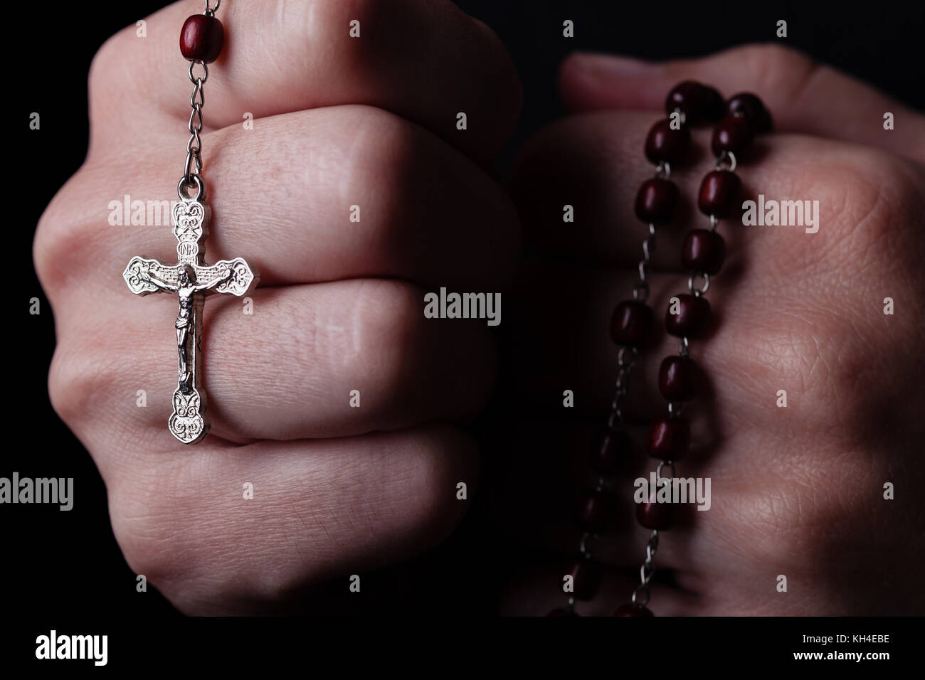 Female hands praying holding a rosary with Jesus Christ in the cross or Crucifix on black background. Woman with Christian Catholic hand faith Stock Photo