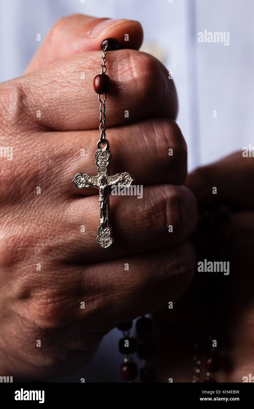 Male hands praying holding a rosary with Jesus Christ in the cross or Crucifix on black background. Mature man with Christian Catholic religious faith Stock Photo