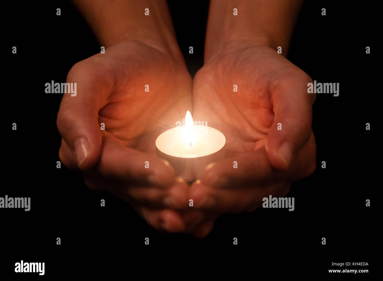 Hands holding and protecting lit or burning candle candlelight on darkness. Black background. Concept for prayer, praying, hope, vigil, night watch Stock Photo