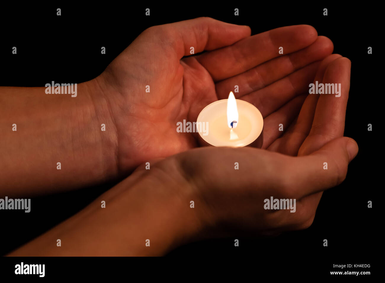 Hands holding and protecting lit or burning candle candlelight on darkness. Black background. Concept for prayer, praying, hope, vigil, night watch Stock Photo