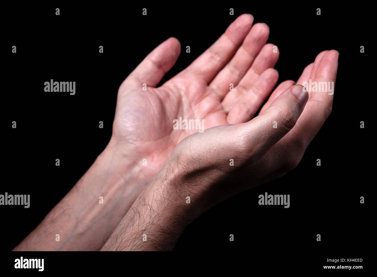 Male hands praying with palms up arms outstretched. Black background. Close up of man hand. Concept for prayer, faith, religion, religious, worship Stock Photo