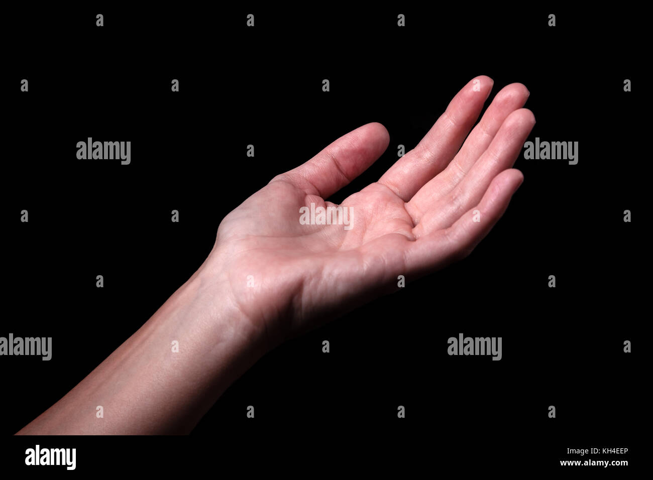 Female hand reaching with palms up. Concept for begging, asking, needing, salvation, rescue, friendship, guidance, help, helping. Black background. Stock Photo