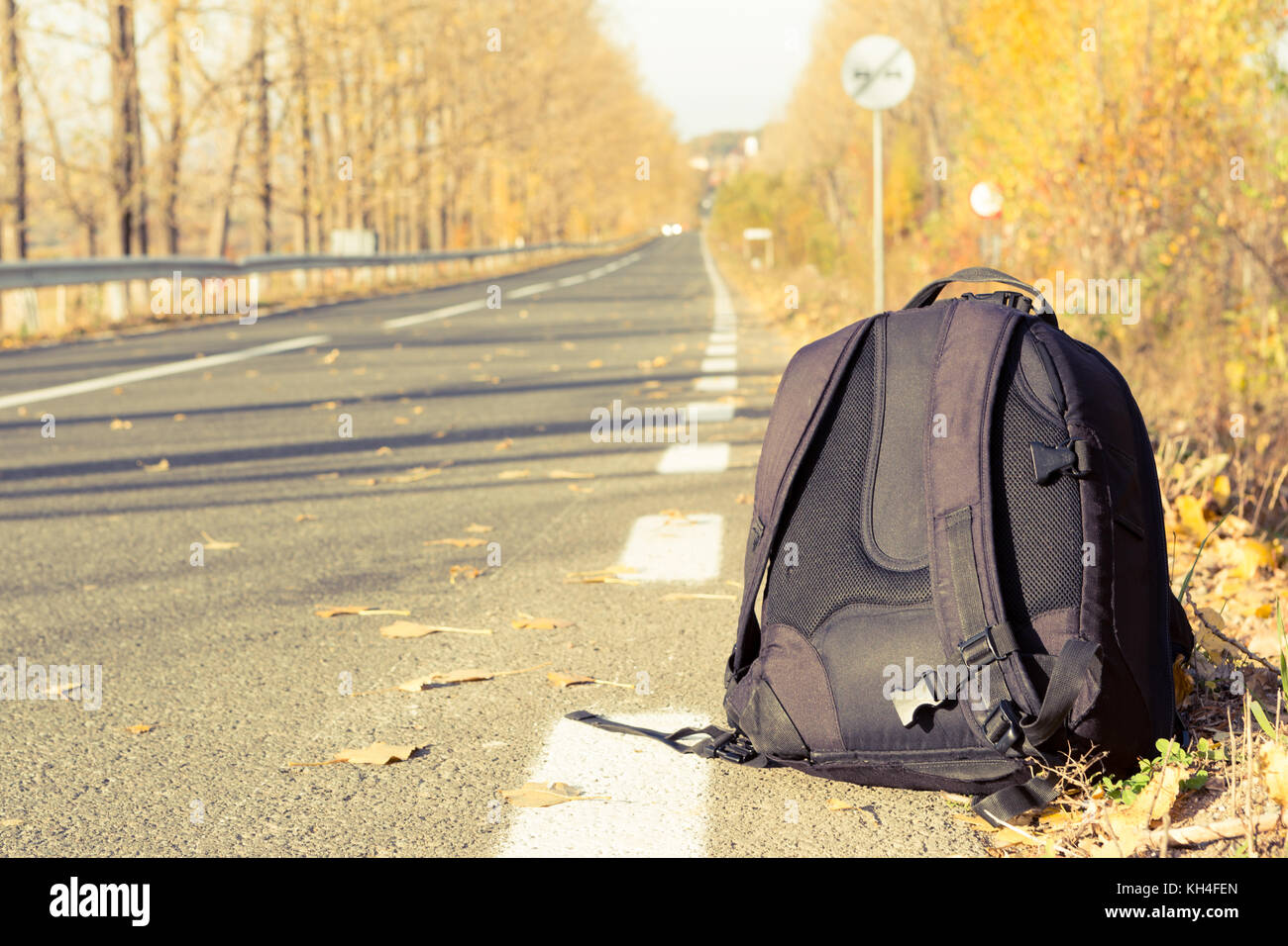 Backpack on the side of the road as travel concept in a sunny day of autumn or fall Stock Photo