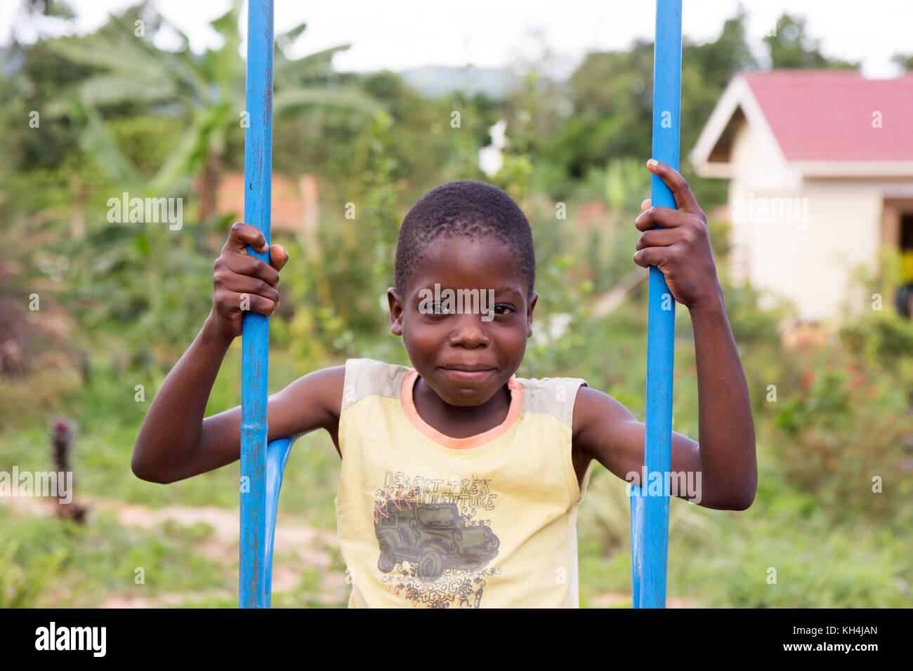 A smiling 13-year old Ugandan boy swinging on a colorful swing Stock Photo