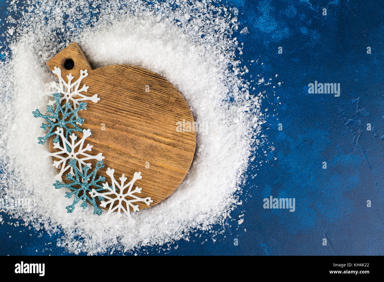 Dark blue background with a rouns board and some sparkling snowflake decorations Stock Photo